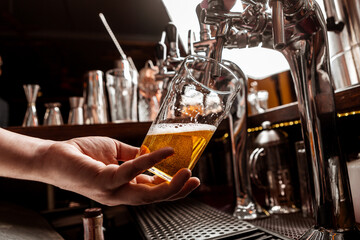 Pour a pint of beer. Bartenders hand holds glass and takes drink from tap