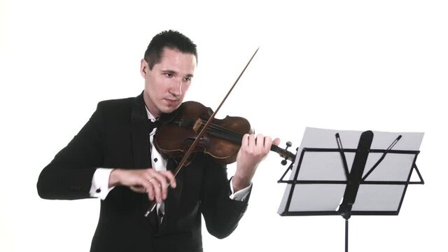 young guy in a tuxedo performs a beautiful slow composition on notes on a classical violin. Isolated. Medium long shot