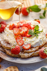 Waffles with the addition of whipped cream and fresh strawberries poured with honey, close-up view