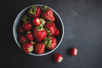 Fresh ripe tasty strawberries in a black plate on a gray wooden background. Two bast bins lie side...