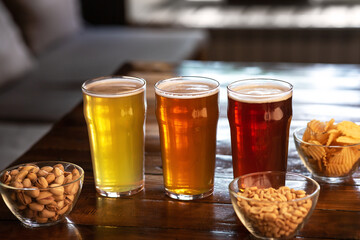 Ale, lager and beer in glasses. Pistachios, nuts and chips in glass plates on table