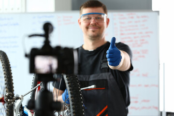 Happy male worker in special clothes repairing a bicycle and shooting video content