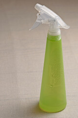 A plastic sprayer with water drops on the side surface stands on a plane covered with a linen cloth