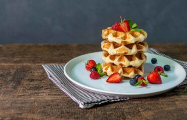Homemade waffles with mixed berries,blueberry,raspberry,strawberry in white plate on wood table.