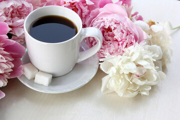 White cup with coffee and tender peonies on a white background. Close-up. Horizontal photo.