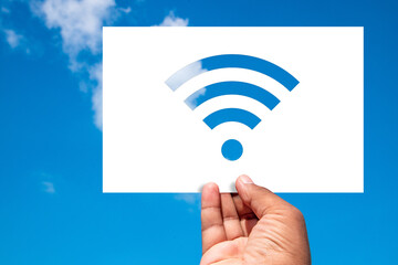 Wireless Concept. Man holds a sheet of paper with wireless Wi-Fi shaped cut-out against the blue sky.