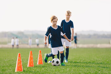 Boys training unit on soccer field. Young footballers practice dribbling skills on the grass pitch. Kids running between red soccer training cones. Summer soccer camp for children team © matimix