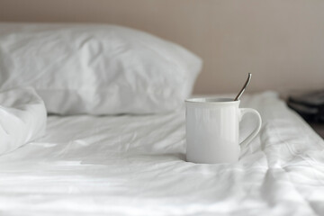 Fototapeta na wymiar White coffee mug with spoon lay on the bed in the morning.