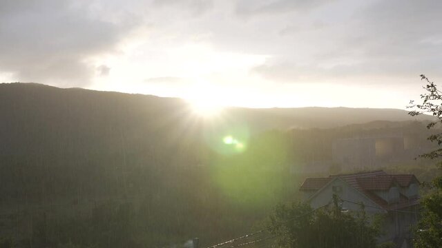 The sun sets over the mountain and it rains blindly over the eco village, glare from the sun.