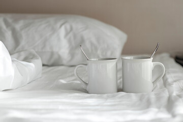 Fototapeta na wymiar Two white coffee mug with spoon lay on the bed in the morning.