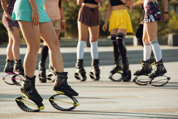 Close up women in sportswear jumping in a kangoo jumps shoes at the street on summer's sunny day. Jumping high, active movement, action, fitness and wellness. Fit female models during training.