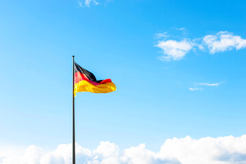 Flag of Germany (Deutschland) flying in the wind, blue sky with clouds. National symbol. European country.