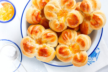Beautiful yeast buns in the shape of flowers in an enameled bowl, top view, selective focus