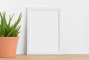 White frame mockup with a aloe vera in a ceramic pot on a wooden table. Portrait orientation.