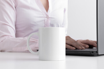 White mug mockup with woman working on a computer.