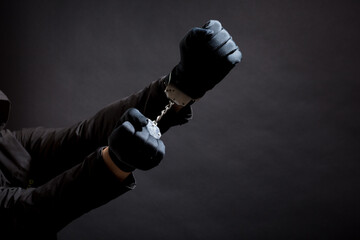 closeup of the hands of a burglar in black gloves with handcuffs on a black background