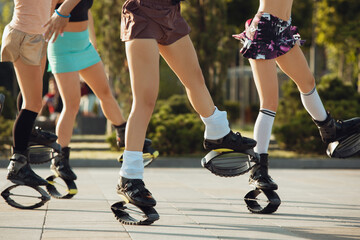 Naklejka premium Close up women in sportswear jumping in a kangoo jumps shoes at the street on summer's sunny day. Jumping high, active movement, action, fitness and wellness. Fit female models during training.