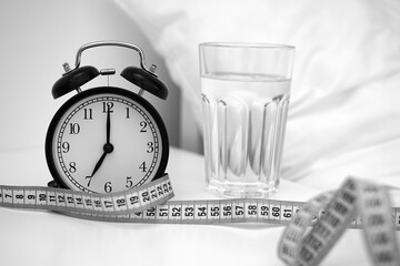 Clear glass of water for drinking on bed in the morning. Weight loss or diet concept. Alarm clock...
