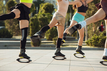 Naklejka premium Close up women in sportswear jumping in a kangoo jumps shoes at the street on summer's sunny day. Jumping high, active movement, action, fitness and wellness. Fit female models during training.