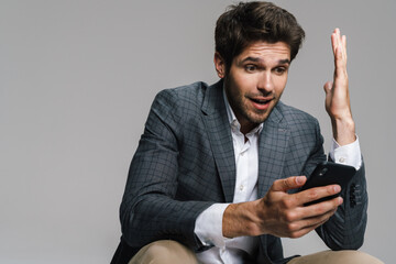 Photo of respectable surprised businessman using cellphone while siting