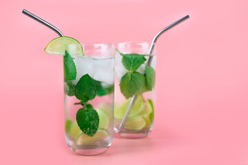 Cocktail alcoholic or non-alcoholic mojito with fresh mint and lime and people on a pink background with eco-friendly straws. Place for text