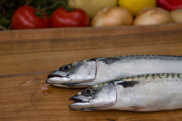 Two whole mackerel fish on a wooden chopping board
