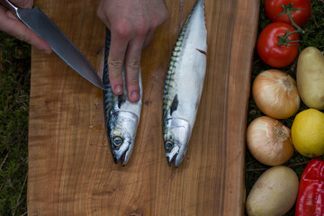 Preparing mackerel fish to cook with vegetables on a wooden chopping board outdoor
