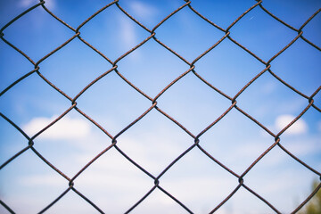 Fototapeta premium Blue sky through rusty wire mesh fence. Blur background, texture. Close up view, wallpaper.