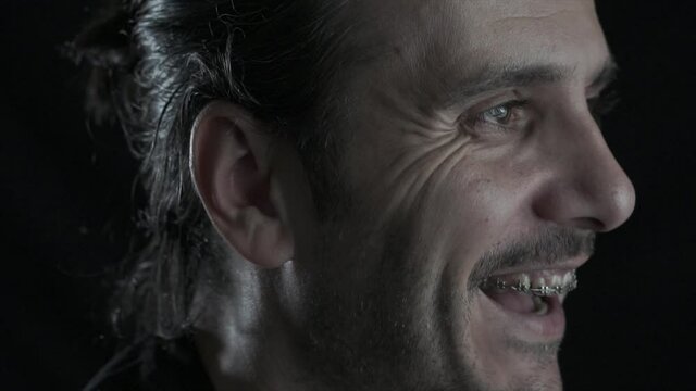 Close up face portrait of long haired young man with brace is smiling to camera. Happy, positive face laughing.