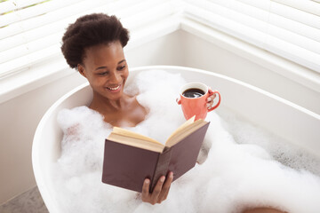 Woman with coffee cup reading book in a bathtub