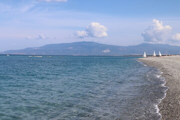 Seascape on a hot summer day, clear calm blue sea, clear sky, pebble beach, catamarans with sails...