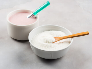 Collagen protein powder in bowl with wooden spoon on marble table. Adding collagen supplement to strawberry yogurt