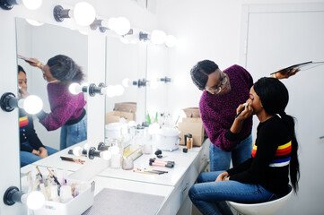 African American woman applying make-up by make-up artist at beauty saloon.