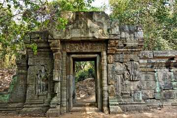 The wall of the ancient castle is dilapidated. On the stones are bas-reliefs, carvings, ornaments. The doorway is preserved, this is the passage from the jungle to the jungle. Cambodia, Angkor. UNESCO
