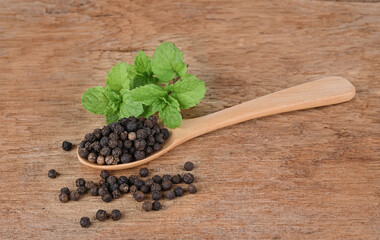 Black pepper in a wooden spoon in wooden background