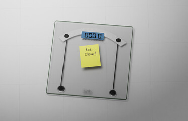 conceptual and modern still of yellow handwritten posit note saying eat clean stuck on bathroom scale in weight loss dieting and healthy nutrition concept