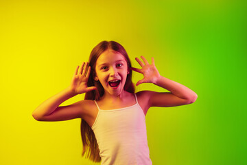 Framing, selfie. Little caucasian girl's portrait isolated on gradient studio background in neon light. Concept of human emotions, facial expression, modern gadgets and technologies, sales, ad