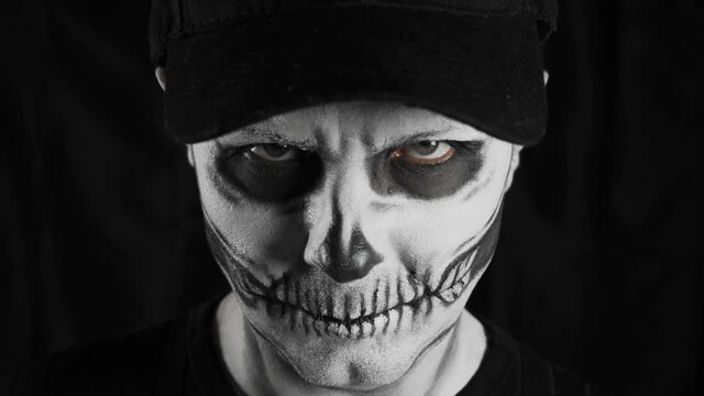 Man with make-up skeleton and black cap on a dark background. Halloween or horror theme. High quality 4k footage