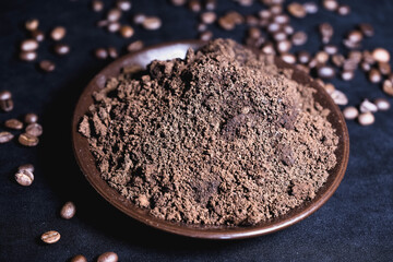 The remains of ground coffee after brewing lie on a saucer and next to the coffee beans