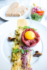 Traditional beef tartar served with a raw egg on top, onion and cucumber in white plate ready to be eaten