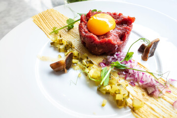 Traditional beef tartar served with a raw egg on top, onion and cucumber in white plate ready to be eaten