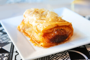 Delicious Greek sweet pastry named Galaktoboureko, made of semolina custard in filo, served with honey in white plate.