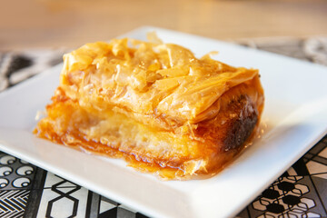 Delicious Greek sweet pastry named Galaktoboureko, made of semolina custard in filo, served with honey in white plate.