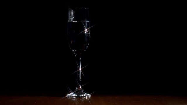 Sparkling cristal clear glass of champagne with transparent liquid inside on a revolving surface and dark background