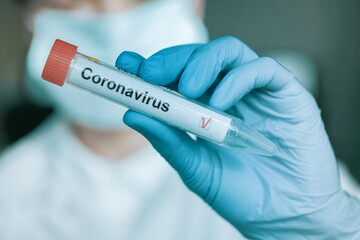 young woman in medical face protection mask and gloves holds a test tube with a coronavirus test. indoors on laboratory background