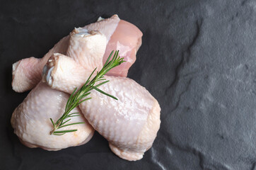 Close up of fresh rare chicken drumstick and rosemary on  black stone  background.