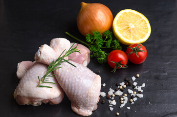Close up of fresh rare chicken drumstick and rosemary with  onion, parsley tomato lemon and seasoning  on  black stone  background.
