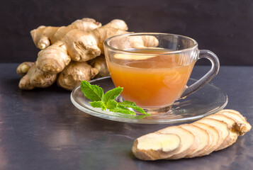 Hot Ginger juice  and mint with root and slices of ginger  on black stone background. Hot Ginger juice can helps warming body.