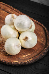 white onions on a wooden board on black background
