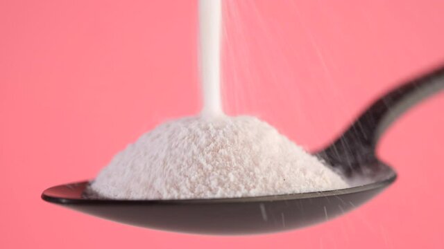 pouring collagen powder in black spoon. pink background closeup. Natural beauty and health supplement